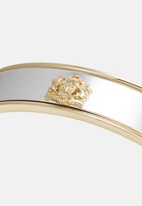 Gullfarget armbånd med en polert sølvstripe og et fremtredende preget design i midten, som fremviser intrikate detaljer og tekstur.