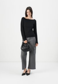 Maglietta nera a maniche lunghe, pantaloni cargo grigi a gamba larga con tasche e una piccola borsa nera. Il modello indossa tacchi neri a punta.