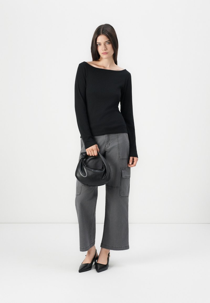 Maglietta nera a maniche lunghe, pantaloni cargo grigi a gamba larga con tasche e una piccola borsa nera. Il modello indossa tacchi neri a punta.