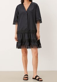 Černé bavlněné šaty s výstřihem do V, krátkými rukávy a krajkovým lemováním. Mají dvouvrstvý volánový design na spodním okraji. Hladká textura, volný střih.