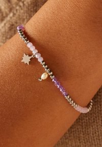 Beaded armband met zilveren accenten, paarse en lichtroze kralen, en een kleine zilveren ster charme. Gemarmerde huid op de achtergrond.