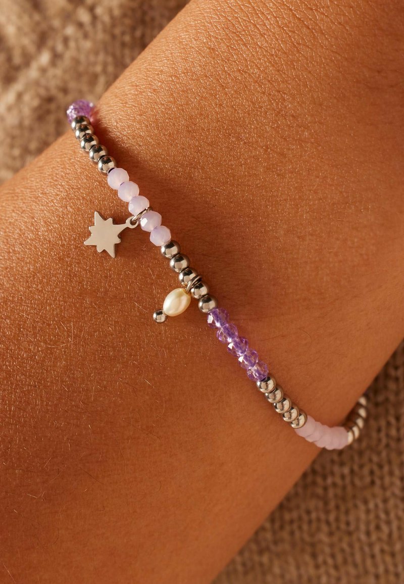 Beaded armband met zilveren accenten, paarse en lichtroze kralen, en een kleine zilveren ster charme. Gemarmerde huid op de achtergrond.