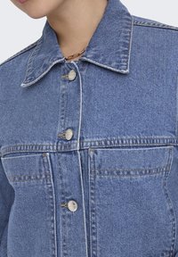 Jeansjacka i ljusblått med klassisk krage, knappstängning fram och två bröstfickor. Har synlig sömnad och metallknappar.