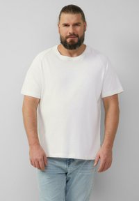 Witte katoenen T-shirt met korte mouwen, een ronde hals en een relaxte pasvorm, gecombineerd met lichtblauwe jeans. Zachte textuur en eenvoudig ontwerp.