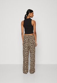 Crop top noir à côtes avec un ourlet festonné associé à un pantalon large à taille haute en imprimé léopard beige et noir.