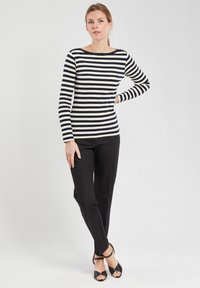 Maglietta a maniche lunghe a righe in blu navy e crema, con scollatura a barca. Abbinata a pantaloni neri attillati e sandali neri con tacco.