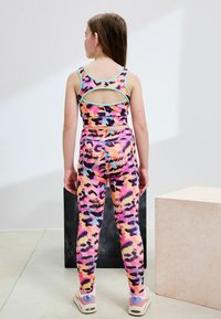 Ensemble brassière de sport et leggings dans un imprimé léopard multicolore vibrant. Comprend un dos découpé et une ceinture élastique pour le confort.