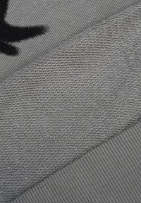 Zbliżenie na rękaw szarego swetra z dzianiny, ukazujące ściągacz oraz szczegóły faktury tkaniny w różnych wzorach dziania.