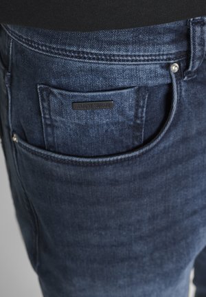 Dunkelblaue Jeansrückseite mit einer kleinen schwarzen Etikette mit der Aufschrift "Antony Morato", die oberhalb der Tasche aufgenäht ist.