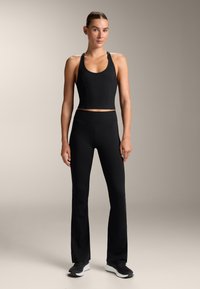 Set sportiv negru, format dintr-un top scurt cu bretele subțiri și pantaloni aderenti cu bucle. Fabricat dintr-un material neted și elastic, cu cusături decorative.