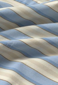 Tissu doux avec des rayures horizontales bleu clair, beige et blanc, formant de légers plis et ombres.