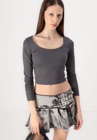 Gray long-sleeve crop top paired with a pleated black-and-gray skirt featuring buttons and a distressed texture.