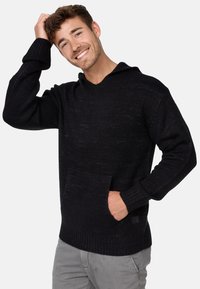 Sudadera negra de punto con escote en V, mangas largas, puños acanalados y un bolsillo frontal. Tejido texturizado con sutiles variaciones de tono.