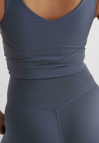 Grått treningstøy sett som inkluderer en tettsittende tanktop med V-hals og sømløse, høyt midje leggings med dekorative sømmer og logo.