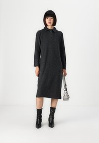 Rochie tricotată gri cu guler, mâneci lungi și o siluetă ajustată. Asortată cu cizme negre cu toc și o geantă argintie.