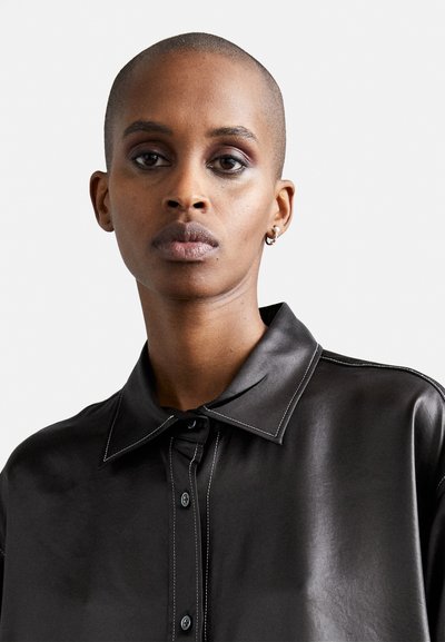 Black leather shirt with a classic collar, button front, and contrasting white stitching detail. Smooth texture and relaxed fit.