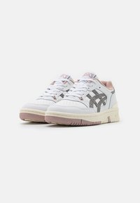 Zapatillas blancas con parte superior de cuero, detalles en gris y toques de rosa. Presenta perforaciones en la puntera y una suela de goma texturizada.