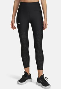 Mallas deportivas negras con una cinturilla alta, que presentan un patrón texturizado en los laterales, combinadas con zapatillas deportivas negras.