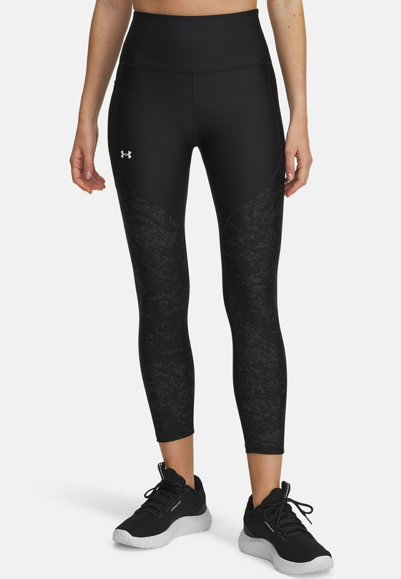 Mallas deportivas negras con una cinturilla alta, que presentan un patrón texturizado en los laterales, combinadas con zapatillas deportivas negras.