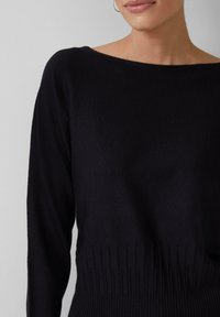 Schwarzer gestrickter Pullover mit weitem Boots-Ausschnitt, langen Ärmeln und geripptem Saum. Hergestellt aus einem weichen, dehnbaren Stoff.