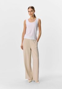Hvid ribbet tanktop parret med beige vide bukser med afslappet fit og lommer, sat mod en ensfarvet hvid baggrund.