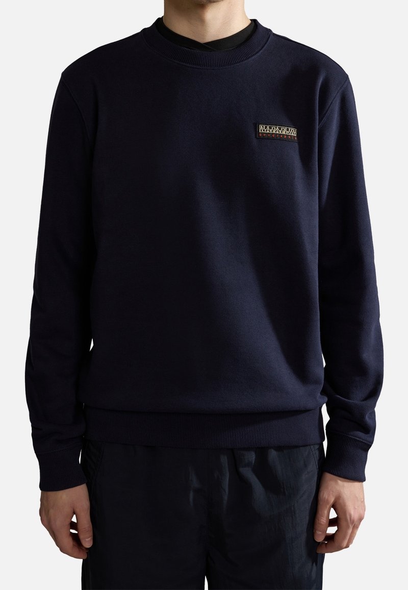 Felpa blu navy con scollo rotondo, polsini e orlo a coste. Presenta una piccola toppa con logo ricamato sul petto. Tessuto morbido, vestibilità casual.