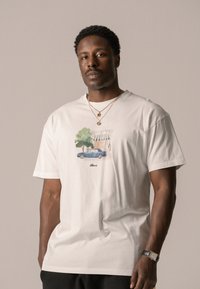 White cotton t-shirt featuring a detailed graphic of a blue car and green tree, with a small text logo beneath the illustration.