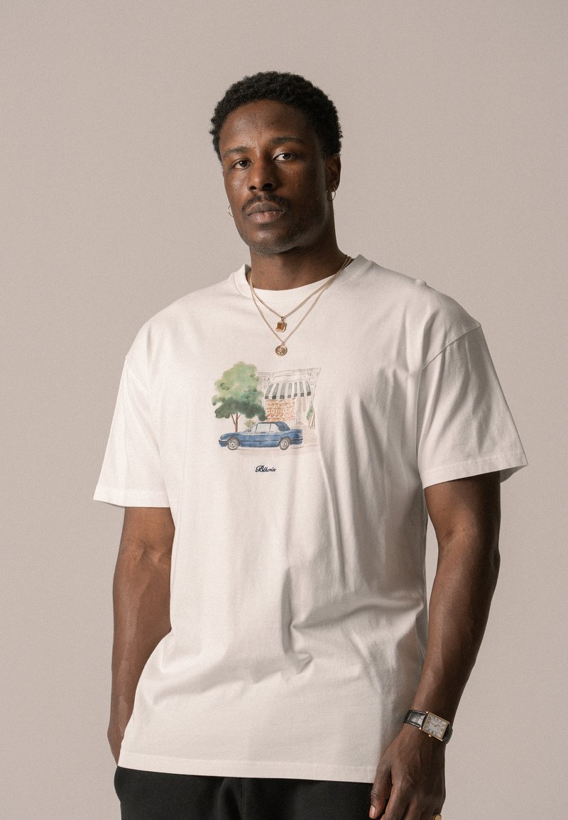 White cotton t-shirt featuring a detailed graphic of a blue car and green tree, with a small text logo beneath the illustration.