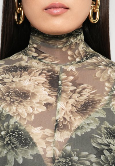 Primer plano de una persona que lleva grandes pendientes de aro de oro y una blusa de cuello alto sheer con estampado floral.