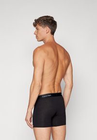Melnas kokvilnas bokseršortus ar Calvin Klein logo uz mīksta jostas, kurai ir pieguļoša forma un gluda tekstūra.