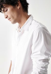 Camisa blanca de algodón con cuello clásico, mangas largas y textura suave, con detalles de botones en la parte delantera.