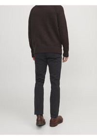 Ciemnobrązowy sweter z dzianiny z prążkowanymi mankietami i ściągaczem, w połączeniu z wąskimi czarnymi spodniami. Stylizację uzupełniają brązowe skórzane buty.