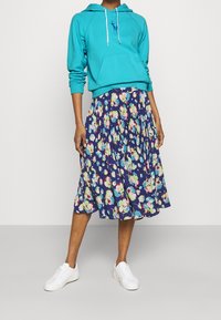 Turkos hoodie med en frontficka, kombinerad med en marinblå blommig midiklänning med veckad design, bärs med vita sneakers.