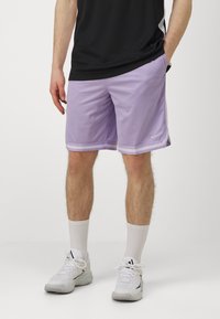 Lilla sportshorts med hvide striber i kanten, lavet af letvægtsstof. Båret med en sort skjorte og hvide sportsko.