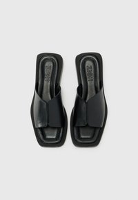 Svarta slidesandaler med en slät läderöverdel, öppen tå-design, låg blockklack och rektangulär sula. Varumärket "ZIGN" präglat på insidan.