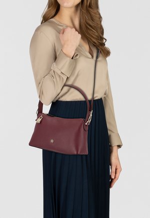 Sac à main en cuir bordeaux à finition texturée, doté d'une poignée courte et d'une bandoulière ajustable, fermé par un fermoir doré.