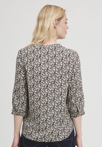 Bloemige blouse met driekwart mouwen, met een marineblauwe achtergrond en kleine witte, gele en bruine bloemen. Zachte stoftextuur, ronde halslijn.