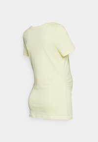 T-shirt amarelo pálido de manga curta, feito de algodão macio. Apresenta um corte descontraído com detalhe franzido nas laterais e um decote redondo.