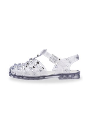 Sandal in gel trasparente con numerosi ritagli circolari, dettagli con borchie e una fascia regolabile. Suola texturizzata per aderenza e stabilità.