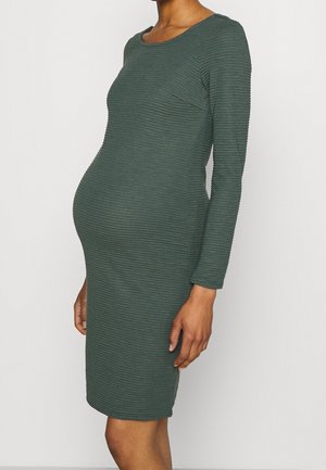 Zwangerschapsjurk van donkergroen ribstof, met lange mouwen, ronde hals, nauwsluitend ontwerp, tot op de knie en met textuurdetails op het oppervlak.