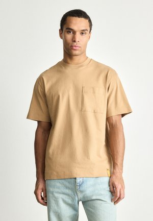 Beige cotton t-shirt with a crew neck, short sleeves, and a left chest pocket. Features a small label on the side hem.