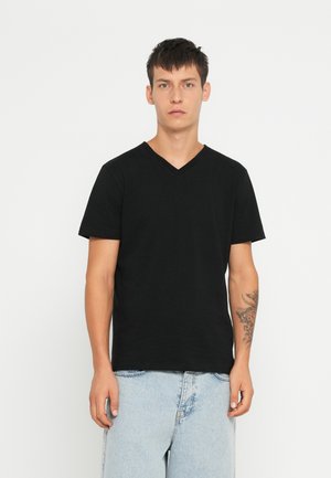 Tricou negru cu decupaj în V confecționat din bumbac, cu mâneci scurte, croială lejeră, purtat cu pantaloni șort din denim albastru deschis.