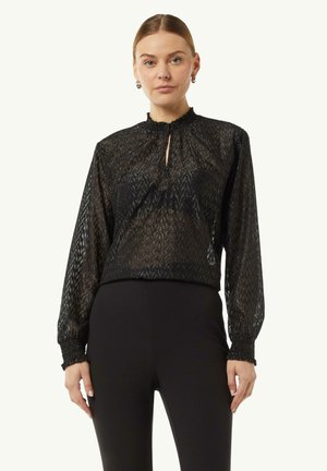 Black blouse with a textured, patterned design, high collar, keyhole opening, and elasticized cuffs, worn with black fitted pants.
