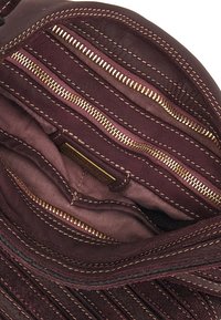 Interno della borsa in pelle marrone con molte tasche con zip e foderato di un bordeaux scuro. Presenta cerniere in tono oro e cuciture a contrasto.