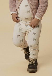 Leggings côtelés ivoire avec un motif de nœud, associés à un cardigan en tricot rose clair et des bottes à lacets marron. Design simple, texture douce.