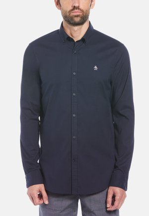Navy blue long-sleeve shirt with a button-down collar, featuring a small white logo on the left chest and matching buttons. Smooth fabric texture.