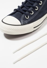 Námořnické semišové vysoké tenisky s bílým gumovým špičákem, černým pruhem a bílými tkaničkami. Podešev má texturovaný grip.