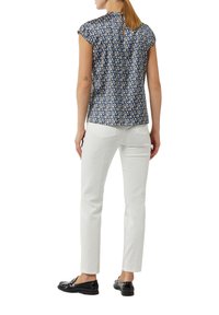 Kurzärmlige, gemusterte Bluse in Marineblau mit cremefarbenem und gelbem geometrischem Design, Rückenschlitzdetail. Kombiniert mit weißen Hosen und schwarzen Schuhen.