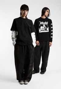 Svart oversized t-skjorte lagdelt med en langermet hvit skjorte. Svart grafisk hettegenser med hvit trykk. Løse svarte bukser og casual sko.