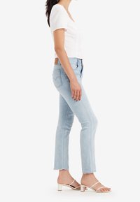 Jeans ajustados de color azul claro con una cintura alta, dobladillo deshilachado y parche de cuero en la parte posterior. Combinados con una blusa blanca de manga corta y tacones con tiras.
